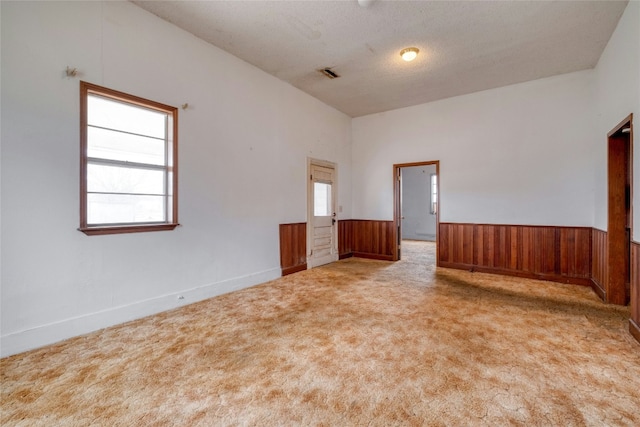 unfurnished room featuring light carpet, wooden walls, visible vents, wainscoting, and a textured ceiling