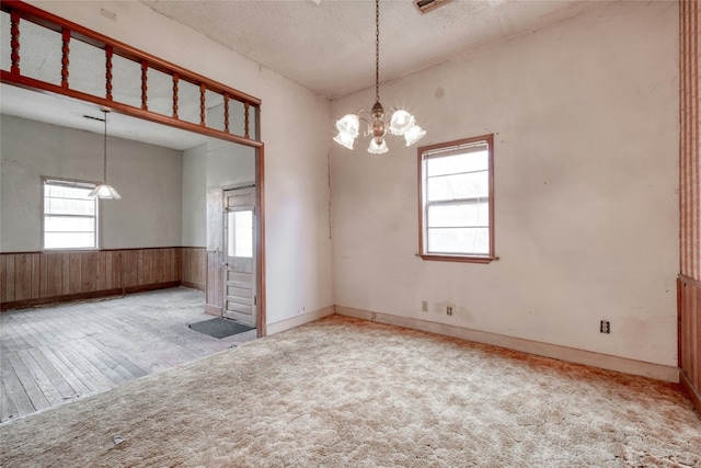 unfurnished room featuring light carpet, wooden walls, wainscoting, an inviting chandelier, and a textured ceiling