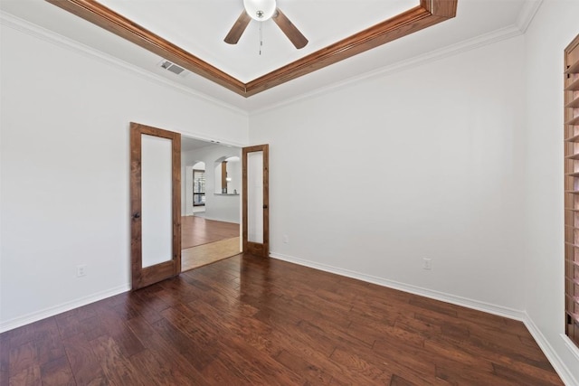 empty room featuring dark wood-type flooring, a raised ceiling, ceiling fan, built in shelves, and ornamental molding