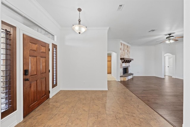 entrance foyer featuring light hardwood / wood-style flooring, ceiling fan, ornamental molding, a fireplace, and a wealth of natural light