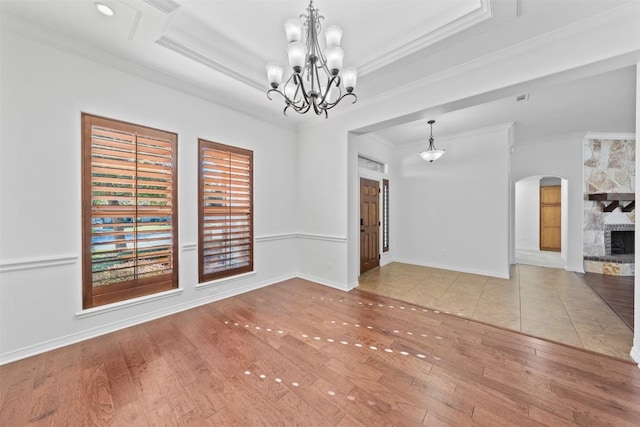 interior space with a raised ceiling, crown molding, an inviting chandelier, light hardwood / wood-style flooring, and a fireplace