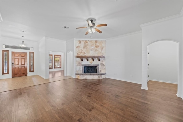 unfurnished living room with a stone fireplace, ceiling fan, ornamental molding, and hardwood / wood-style flooring