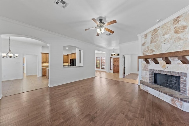 unfurnished living room featuring crown molding, a fireplace, ceiling fan with notable chandelier, and light wood-type flooring