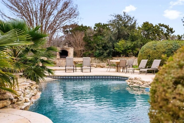 view of pool with a patio and an outdoor stone fireplace