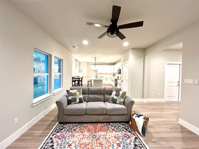 living room with ceiling fan, sink, and light wood-type flooring