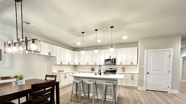 kitchen featuring sink, stainless steel appliances, light hardwood / wood-style floors, decorative light fixtures, and white cabinets