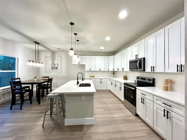 kitchen with stainless steel appliances, sink, a center island with sink, white cabinets, and light hardwood / wood-style floors