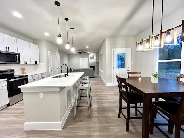 kitchen with a kitchen island with sink, sink, ceiling fan, appliances with stainless steel finishes, and light hardwood / wood-style floors