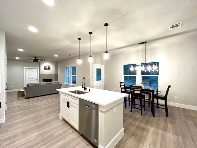 kitchen with pendant lighting, a kitchen island with sink, sink, stainless steel dishwasher, and white cabinetry