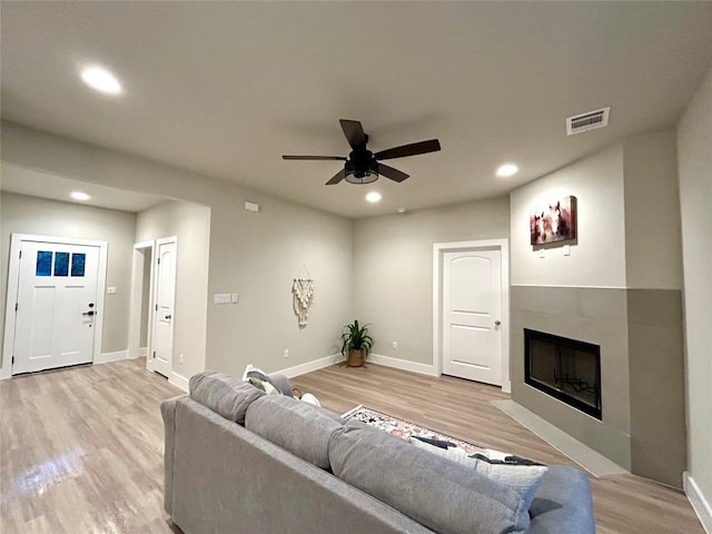 living room with a tile fireplace, ceiling fan, and light hardwood / wood-style floors