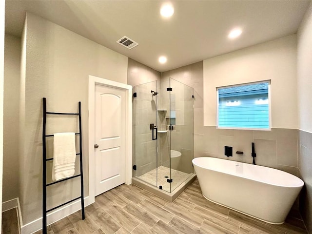 bathroom featuring plus walk in shower, wood-type flooring, and tile walls