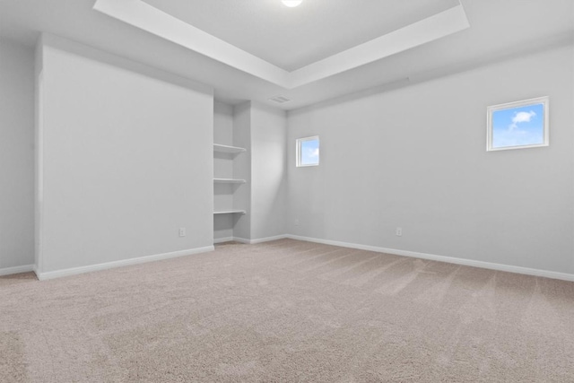 carpeted empty room featuring a raised ceiling, built in shelves, and a healthy amount of sunlight