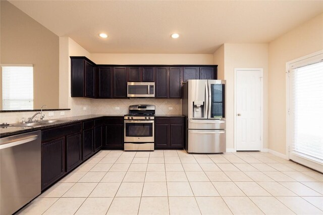 kitchen with appliances with stainless steel finishes, backsplash, sink, dark stone countertops, and light tile patterned flooring