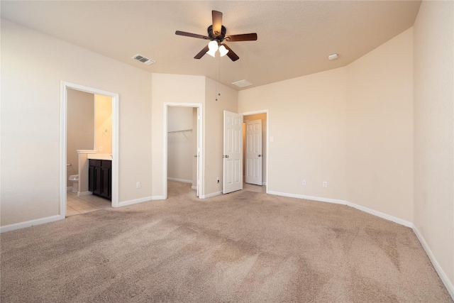 unfurnished bedroom with light carpet, ensuite bathroom, ceiling fan, a spacious closet, and a closet