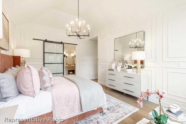 bedroom featuring lofted ceiling, a barn door, wood-type flooring, and an inviting chandelier