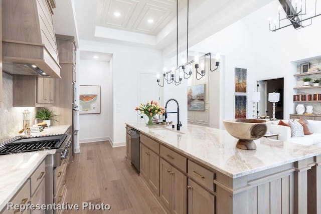 kitchen with hanging light fixtures, light stone counters, an island with sink, light hardwood / wood-style floors, and custom range hood