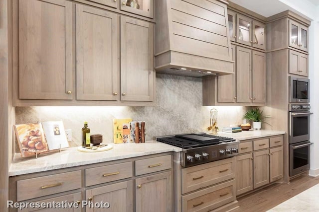 kitchen featuring light stone countertops, light brown cabinetry, premium range hood, stainless steel appliances, and light hardwood / wood-style flooring