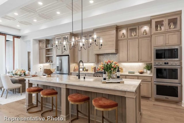 kitchen with appliances with stainless steel finishes, light stone counters, light hardwood / wood-style flooring, and an island with sink