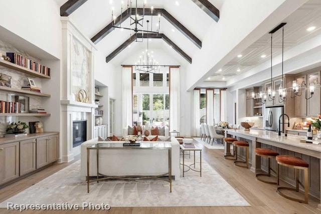 living room with beamed ceiling, light hardwood / wood-style floors, high vaulted ceiling, and a chandelier