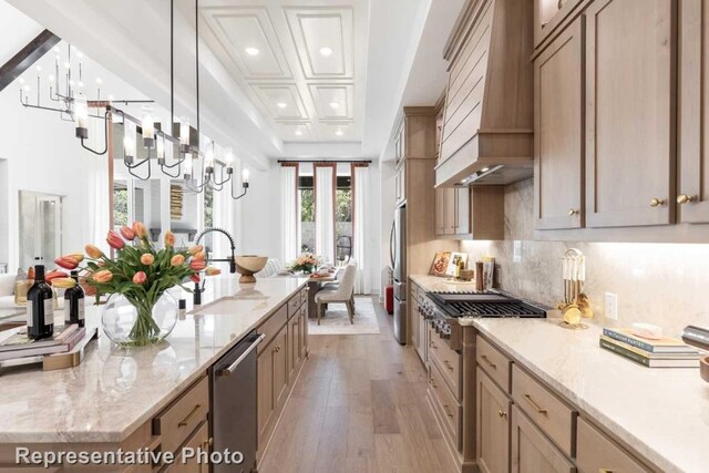 kitchen featuring hanging light fixtures, light hardwood / wood-style flooring, beam ceiling, custom range hood, and stainless steel appliances