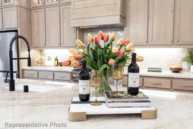 kitchen featuring decorative backsplash, light stone countertops, sink, and custom exhaust hood