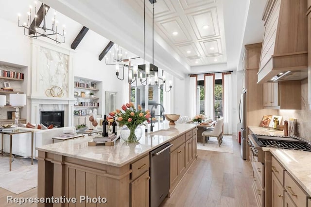 kitchen with a center island with sink, light wood-type flooring, decorative light fixtures, custom range hood, and stainless steel appliances