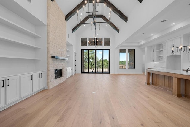 790 Old Stone Rd, Austin, TX 78737 - unfurnished living room with a chandelier, built in features, a stone fireplace, high vaulted ceiling, and light wood-type flooring