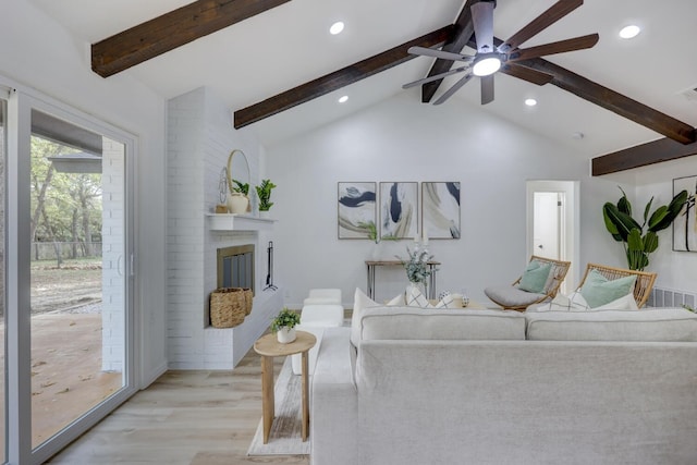 living room featuring vaulted ceiling with beams, ceiling fan, light hardwood / wood-style floors, and a brick fireplace