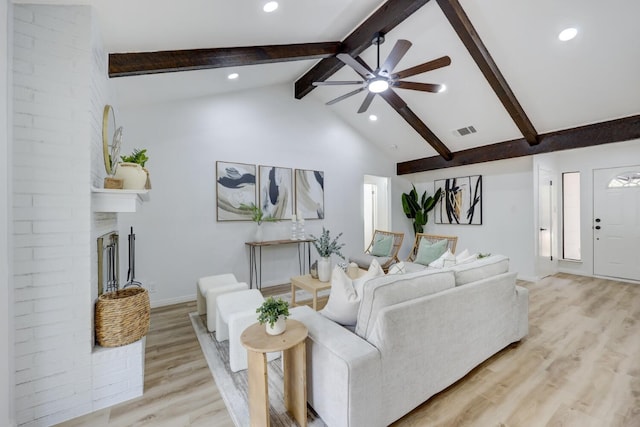 living room with high vaulted ceiling, a brick fireplace, light hardwood / wood-style flooring, ceiling fan, and beam ceiling