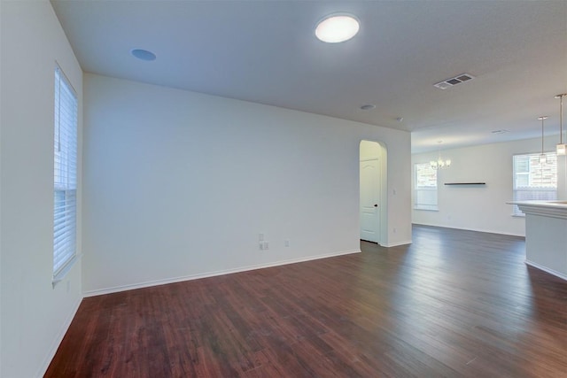 spare room featuring a chandelier and dark wood-type flooring