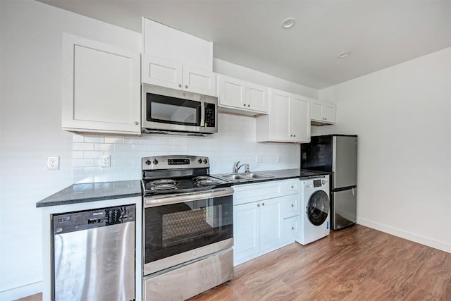 kitchen with appliances with stainless steel finishes, sink, hardwood / wood-style flooring, white cabinets, and washer / dryer