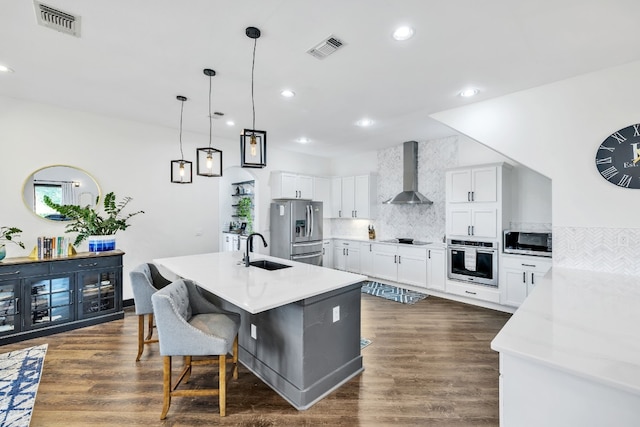 kitchen with appliances with stainless steel finishes, wall chimney exhaust hood, a kitchen island with sink, sink, and white cabinets