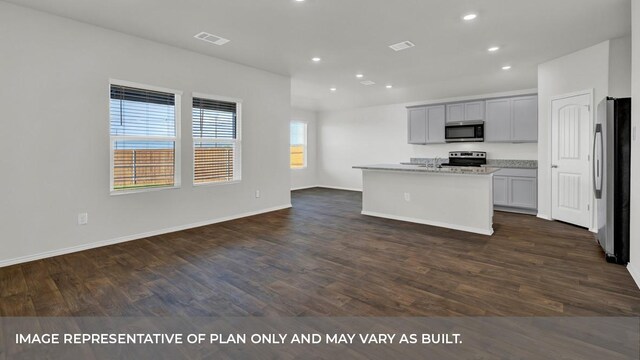 kitchen featuring dark wood-type flooring, gray cabinets, an island with sink, appliances with stainless steel finishes, and light stone counters