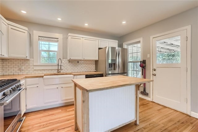 kitchen with white cabinets, sink, light wood-type flooring, appliances with stainless steel finishes, and tasteful backsplash