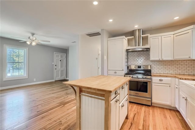 kitchen with a center island, light hardwood / wood-style flooring, wall chimney exhaust hood, white cabinetry, and stainless steel range with gas stovetop