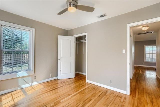 unfurnished bedroom with ceiling fan, a closet, light wood-type flooring, and multiple windows