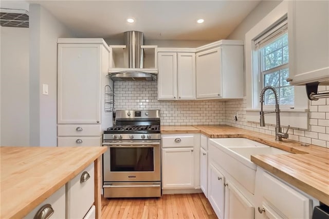 kitchen featuring white cabinets, wall chimney exhaust hood, wooden counters, and stainless steel gas range