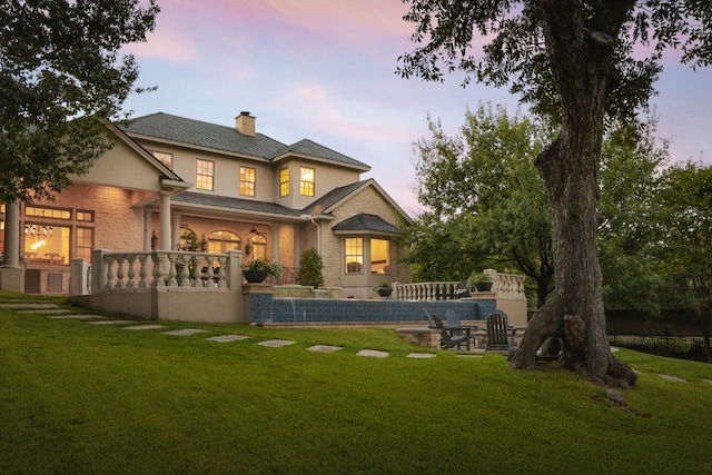 back house at dusk with pool water feature and a yard