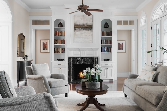 living room featuring ceiling fan, built in features, hardwood / wood-style flooring, a fireplace, and ornamental molding