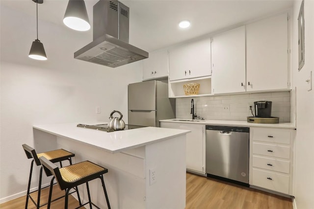 kitchen with a kitchen bar, appliances with stainless steel finishes, island range hood, decorative light fixtures, and white cabinets