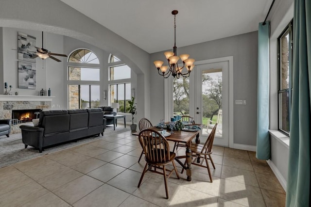 tiled dining space featuring ceiling fan with notable chandelier, a stone fireplace, and a wealth of natural light