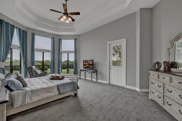 carpeted bedroom featuring a raised ceiling, multiple windows, and ceiling fan