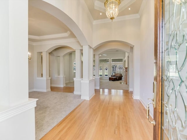 entryway with ornate columns, ornamental molding, a towering ceiling, a notable chandelier, and wood-type flooring