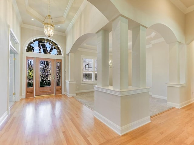 entryway featuring crown molding, light wood-type flooring, a towering ceiling, ornate columns, and a notable chandelier