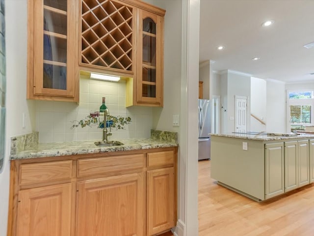 kitchen featuring light wood-type flooring, stainless steel refrigerator, crown molding, and light stone counters