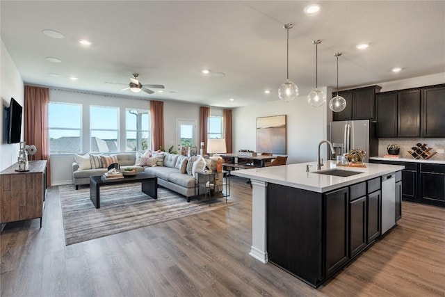 kitchen with sink, stainless steel fridge with ice dispenser, light hardwood / wood-style flooring, decorative light fixtures, and a center island with sink