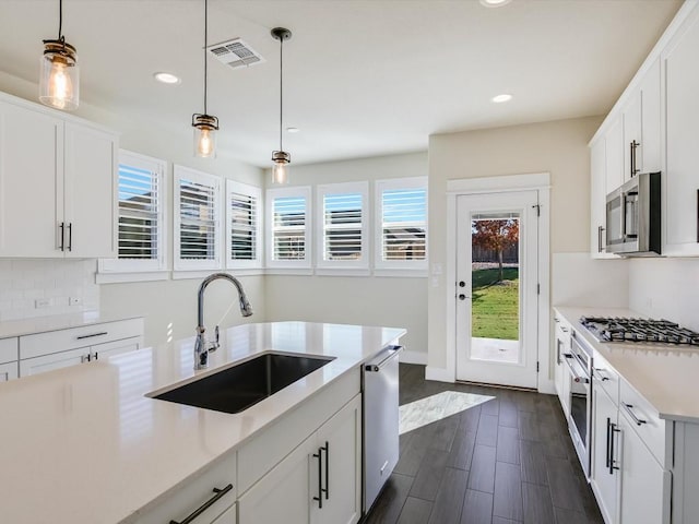 kitchen with white cabinetry, sink, dark wood-type flooring, decorative light fixtures, and appliances with stainless steel finishes