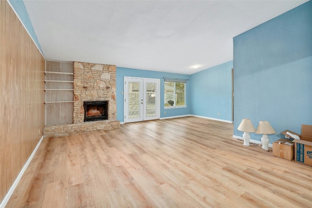 unfurnished living room featuring a stone fireplace, wooden walls, and light hardwood / wood-style flooring