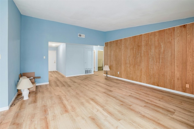 unfurnished room featuring wood walls, light hardwood / wood-style floors, and vaulted ceiling