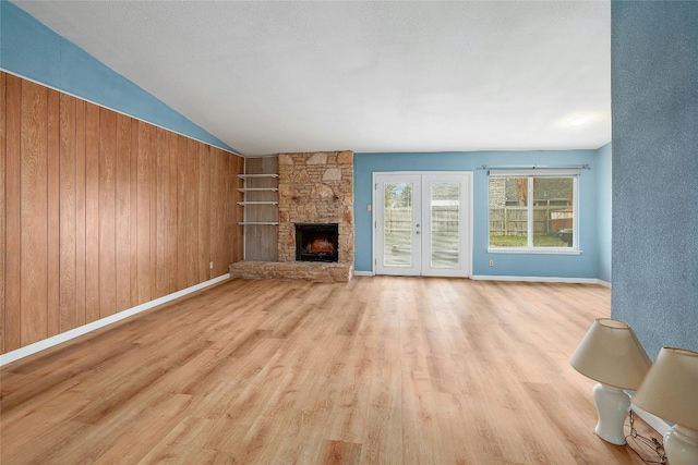 unfurnished living room featuring lofted ceiling, wooden walls, light wood-type flooring, a textured ceiling, and a fireplace